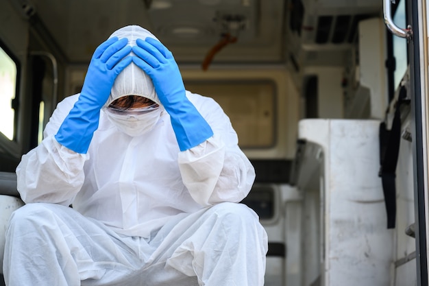 Profissionais de saúde que trabalham em ambulâncias de emergência usando roupas de proteção de epi. assistentes médicos sentam-se tristes e cansados na ambulância.