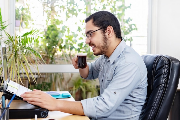 Profissional analisando plano de negócios no laptop Executivo masculino está tomando café enquanto trabalha na mesa