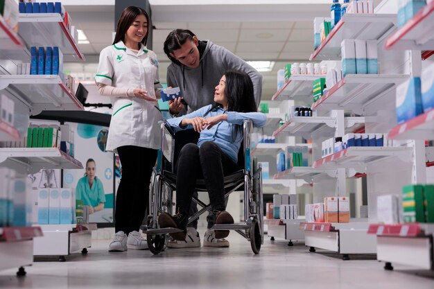 Profissional de saúde dando caixa de comprimidos para mulher e jovem, cliente lidando com deficiência crônica em loja de farmácia. Clientes asiáticos pedindo ao farmacêutico para ajudar com suplementos medicinais.