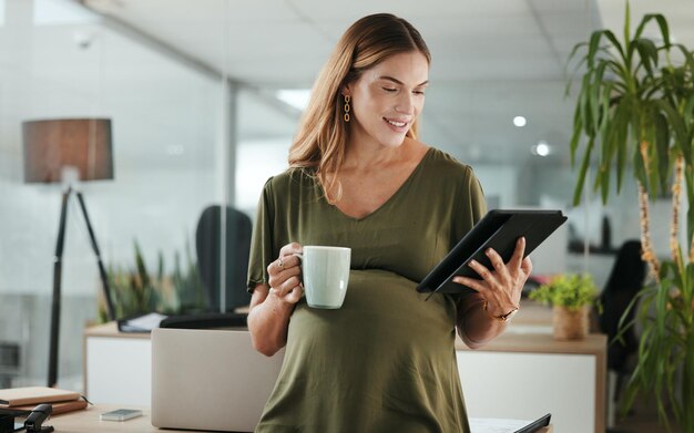 Foto profissional de tablets e mulher de negócios grávida no escritório lê informações na internet xícara de café de maternidade e designer feminina do canadá com gravidez trabalha em tecnologia digital no local de trabalho