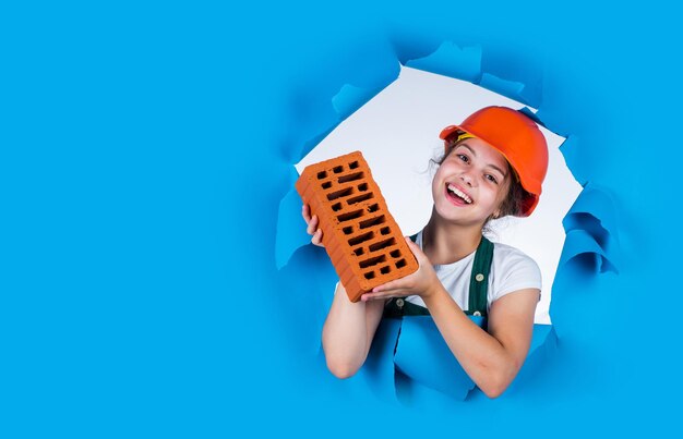 Profissional de verdade. criança usar capacete no canteiro de obras. construtor de menina adolescente com construção de tijolos. filho de pedreiro na reparação de trabalhos. conceito de renovação na oficina. carpinteiro profissional ocupado.