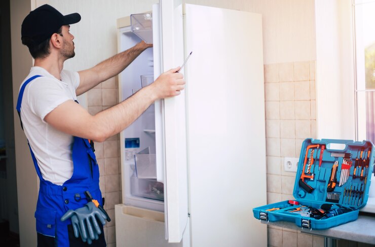 Foto profissional jovem reparador com uniforme de trabalhador e boné com caixa de ferramentas moderna com equipamento está consertando a geladeira na cozinha