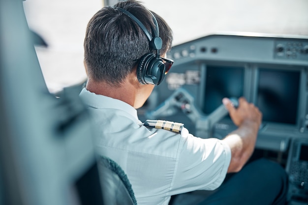 Profissional masculino de uniforme e fones de ouvido está segurando o leme no controle enquanto dirige o jato no trabalho