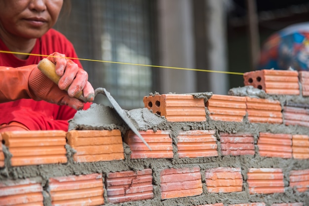 Profissional que instala o tijolo vermelho no canteiro de obras.