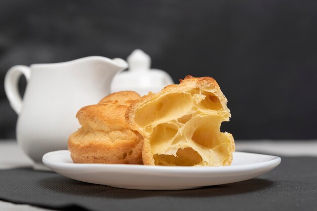 Profiteroles aireados, bocanadas, popovers, canutillos en plato blanco sobre fondo de juego de té.