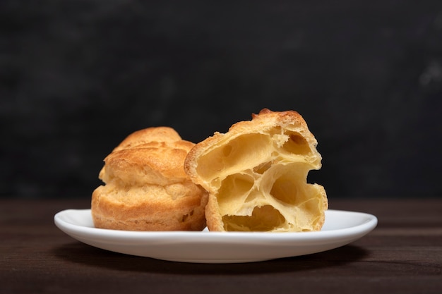 Profiteroles auf Nahaufnahme auf weißer Untertasse, schwarze Wand. Vorbereitung für Eclairs.