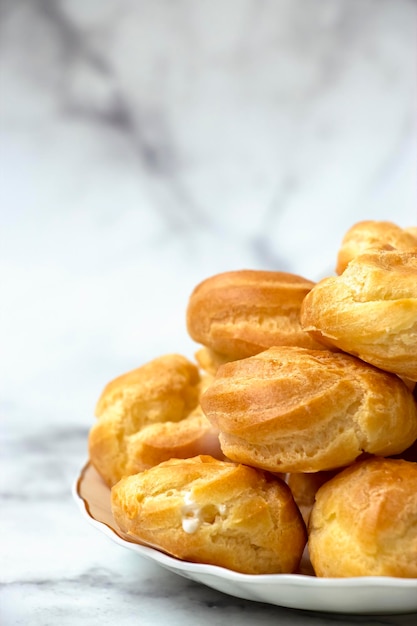 Profiteroles caseiros recheados com chantilly sobre fundo claro de mármore