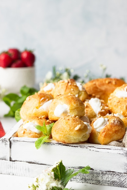 Profiteroles (Choux à la Crème) - Französische Choux-Gebäckbällchen mit Hüttenkäse und Sahne mit Erdbeere, Minze und Tasse Kaffee.