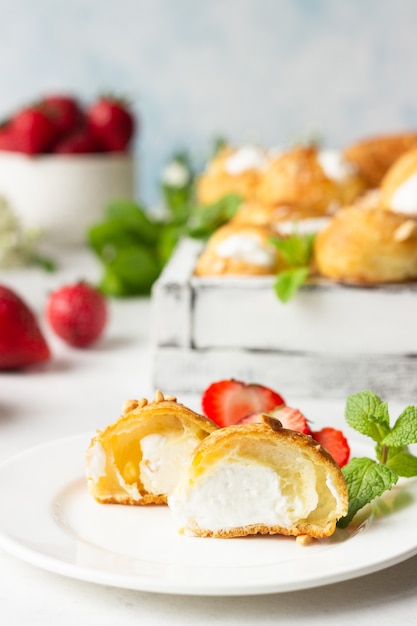 Profiteroles (Choux à la Crème) - Französische Choux-Gebäckbällchen mit Hüttenkäse und Sahne mit Erdbeere, Minze und Tasse Kaffee.