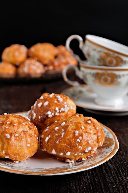 Profiteroles coberto com açúcar e xícara vintage com chá em um fundo escuro