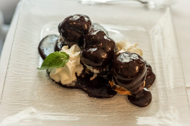 Profiteroles franceses tradicionales bañados en chocolate con crema batida y menta