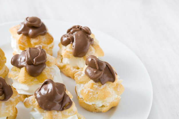 Profiteroles frescos con crema y chocolate en la mesa de madera blanca