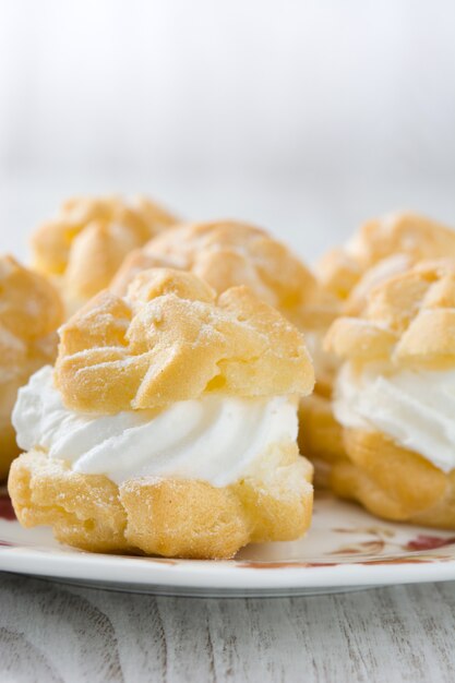 Profiteroles frescos con crema y mesa de madera blanca