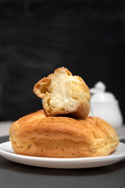 Profiteroles mit Quarkfüllung. Hausgemachtes Backen für Tee. Dessert-Eclairs auf schwarzem Hintergrund. Nahaufnahme.