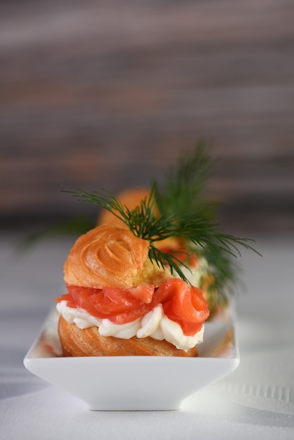 Profiteroles recheados com cream cheese e salmão, decorados com um raminho de endro. Fechar-se