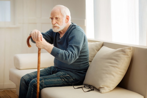 Profundamente en pensamientos. Hombre serio presionando los labios y mirando hacia adelante mientras está sentado en posición semi en la habitación