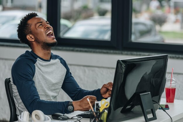 programador afroamericano enojado gestando mientras está sentado en el lugar de trabajo en la oficina