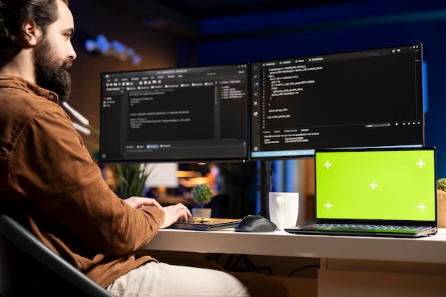 Programador comprobando el código mostrado en los monitores de la computadora utilizando el cuaderno de maqueta