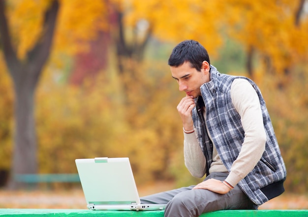 Programador con cuaderno sentado en el parque de otoño