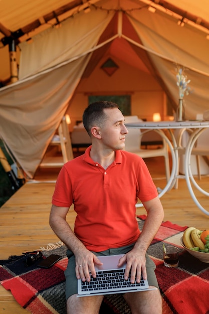 Programador freelancer de homem feliz usando um laptop em uma aconchegante barraca glamping em um dia de verão Barraca de acampamento de luxo para férias ao ar livre e férias Conceito de estilo de vida