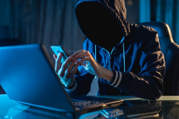 Foto programador hacker anônimo usa um laptop para hackear o sistema no escuro. conceito de cibercrime e banco de dados de hackers