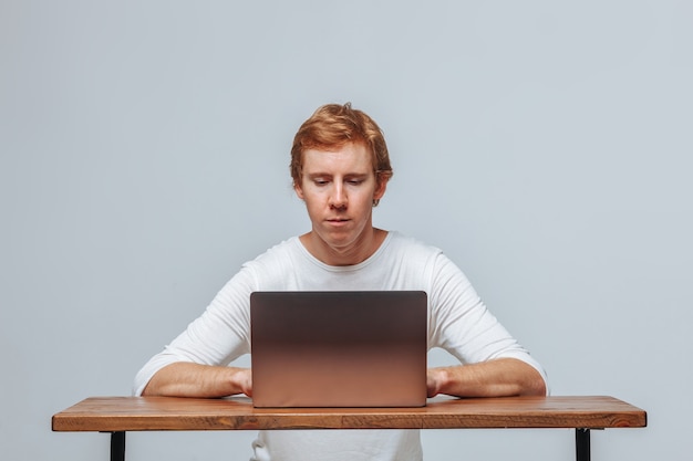 Programador hombre sentado en un portátil sobre un fondo gris claro