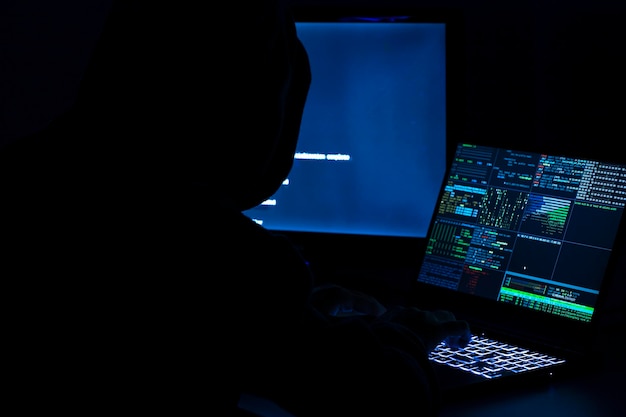 Un programador informático y un hacker imprimen un código en el teclado de una computadora portátil para entrar en un misterioso sistema organizativo