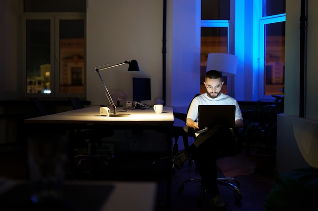 Programador insomne trabaja en la computadora portátil por la noche joven especialista en gafas con estilo de vida nocturno