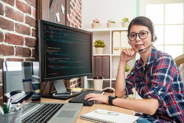 programador joven y guapo que usa un teléfono de cabeza y mira a la pantalla con una sonrisa segura