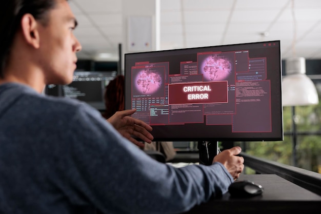 El programador lee el mensaje de error del sistema en el monitor de la computadora, tratando de resolver el problema de alerta de piratería. Desarrollador web que ha pirateado el servidor, trabajando en su sala de oficina de big data.