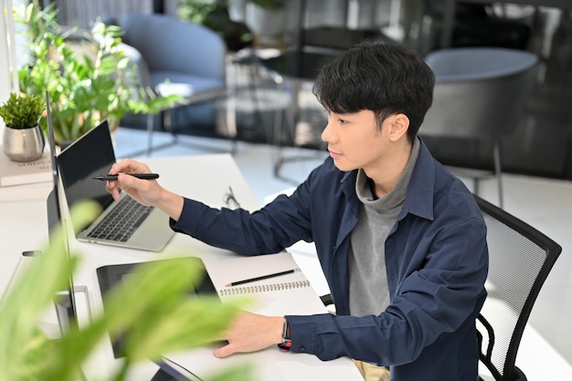 Programador masculino asiático inteligente ou desenvolvedor web trabalhando em sua visão lateral de mesa de escritório