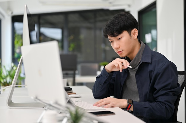 Programador masculino asiático trabajando en el escritorio de su oficina Oficial masculino joven trabajando en su tarea