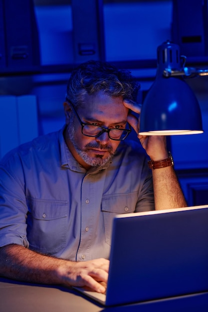 Programador masculino maduro cansado sentado en el lugar de trabajo frente a la computadora portátil