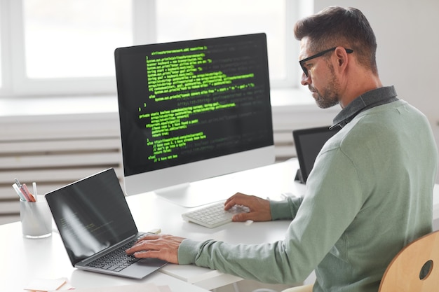 Programador masculino que trabaja en una computadora de escritorio con muchos monitores en la oficina en la empresa de desarrollo de software