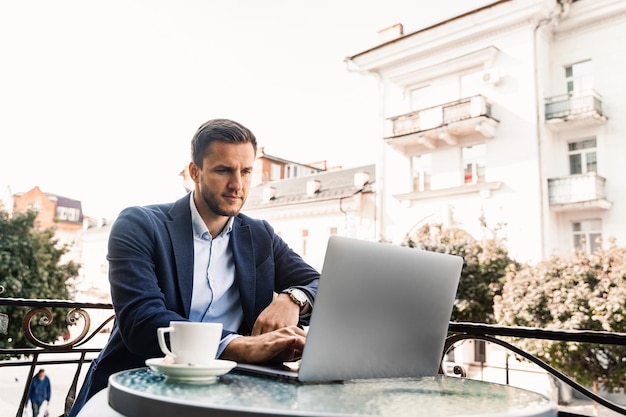 Programador con taza de café está trabajando en línea usando una computadora portátil en la cafetería. Trabajo remoto.