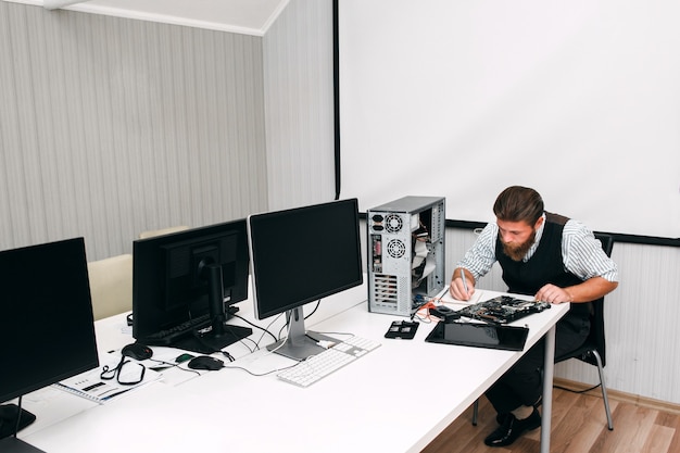 Programador testando equipamentos de trabalho em espaço aberto. O administrador do sistema conduz um inventário de computadores e telas no escritório e anota os resultados no notebook