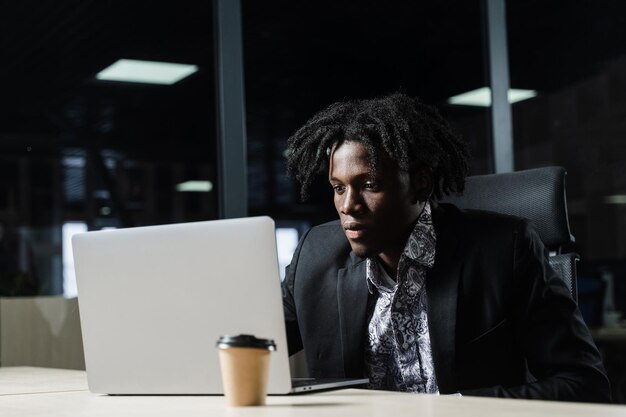 El programador de TI negro está trabajando en una computadora portátil en un espacio de coworking. Hombre africano guapo con laptop en la oficina.