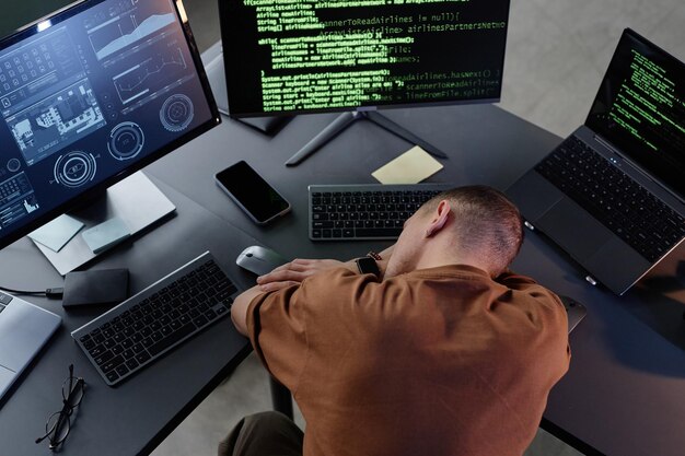 Programador varón cansado tendido en el escritorio de trabajo con computadoras descansando en la oficina