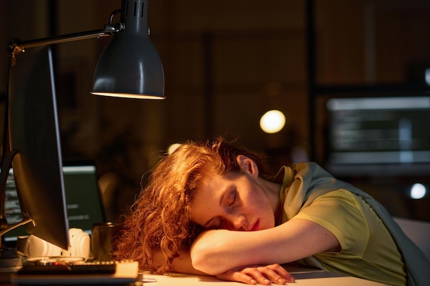 Programadora cansada durmiendo en su lugar de trabajo con una computadora durante su fecha límite en el cargo