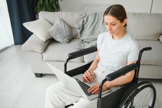 Programadora independiente sentada en silla de ruedas y usando computadoras mientras codifica un juego web en casa