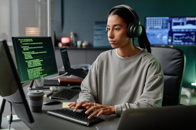 Programadora de Oriente Medio con auriculares centrada en la codificación en la computadora en la oficina