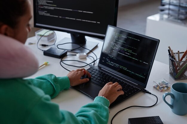 Programadora sentada en su lugar de trabajo con computadoras y escribiendo códigos en una computadora portátil en la oficina