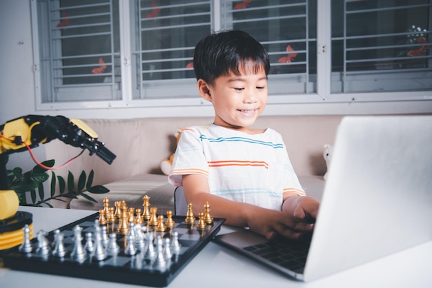 Programmiercode des asiatischen kleinen Jungen zum Robotermaschinenarm auf Laptop für Schachspiel