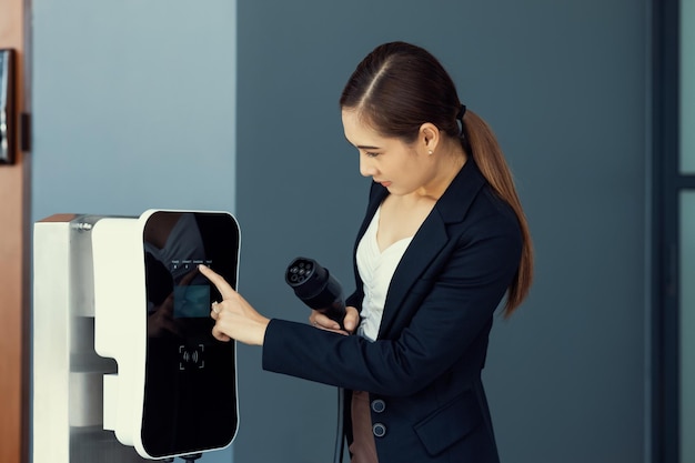 Progressive asiatische Frau mit EV-Stecker an der Ladestation zu Hause