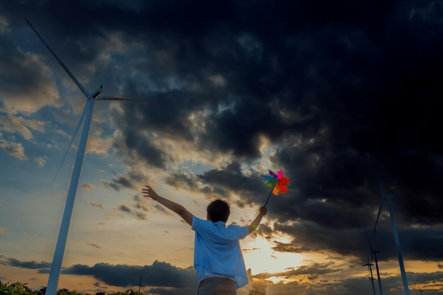 Progressiver junger asiatischer Junge, der mit Windwindrad-Spielzeug im Windturbinenpark spielt