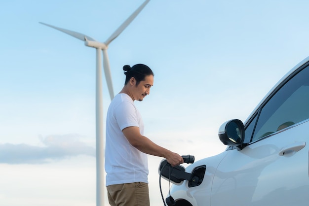Progressiver Mann mit seinem EV-Auto und seiner Windkraftanlage als Konzept für erneuerbare Energien