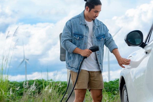 Progressiver Mann mit seinem EV-Auto und seiner Windkraftanlage als Konzept für erneuerbare Energien