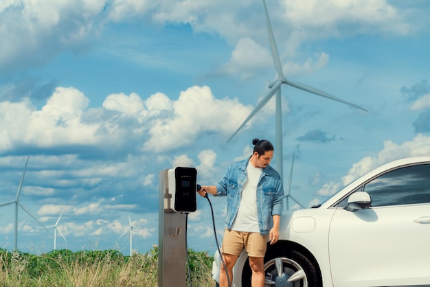 Progressiver Mann mit seinem EV-Auto und seiner Windkraftanlage als Konzept für erneuerbare Energien