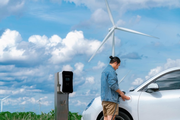 Progressiver Mann mit seinem EV-Auto und seiner Windkraftanlage als Konzept für erneuerbare Energien