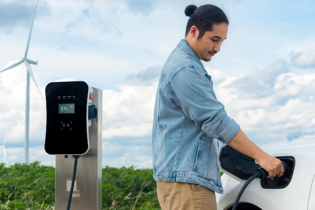 Progressiver Mann mit seinem EV-Auto und seiner Windkraftanlage als Konzept für erneuerbare Energien